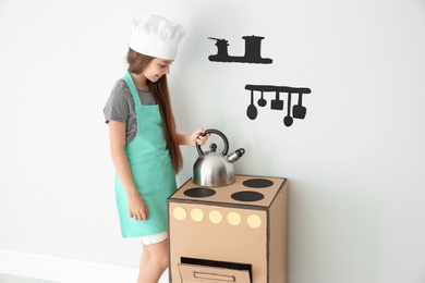 Little child in chef hat playing with carton stove indoors