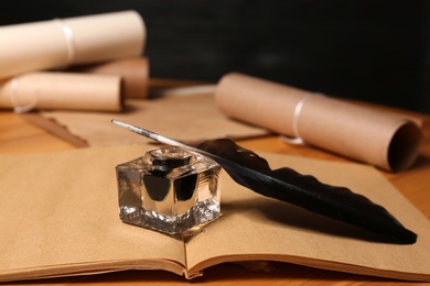 Feather pen, inkwell and open notebook on wooden table