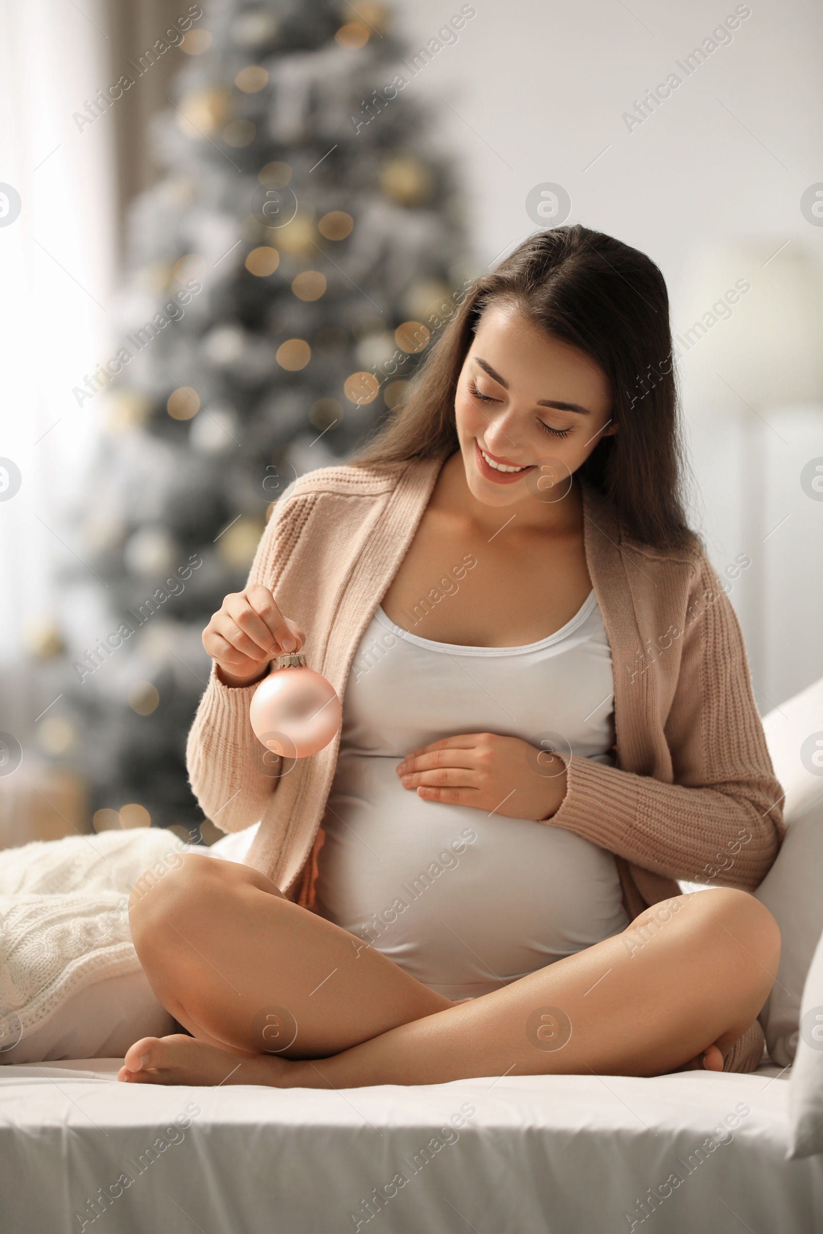 Photo of Happy pregnant woman with Christmas ball on bed at home. Expecting baby