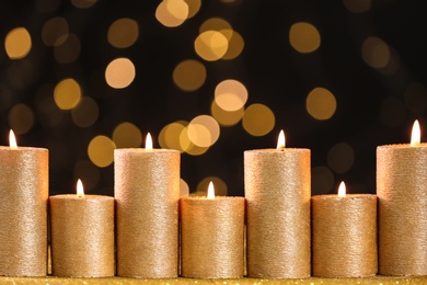 Photo of Golden candles burning on table against defocused lights. Space for text