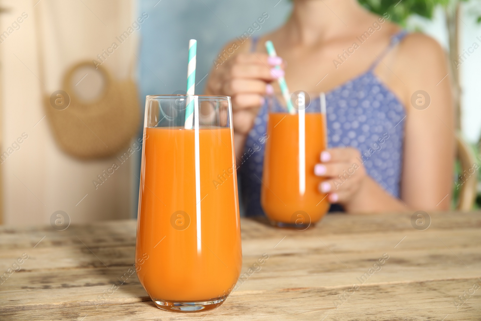 Photo of Woman with drinking fresh carrot juice at wooden table, focus on glass