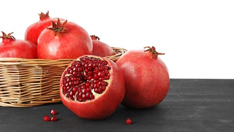 Photo of Fresh pomegranates in wicker basket on black wooden table against white background, space for text