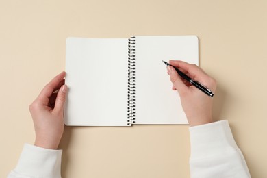 Photo of Woman with pen and notepad on beige background, top view