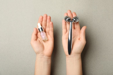 Photo of Woman with metal face roller and cosmetic product on grey background, top view