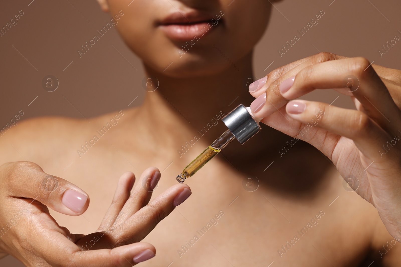 Photo of Woman applying serum onto her finger on brown background, closeup