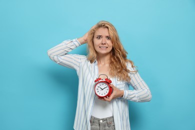 Emotional woman with alarm clock in turmoil over being late on light blue background