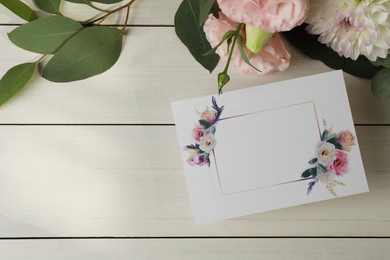 Photo of Blank invitation card, eucalyptus leaves and flowers on white wooden table, flat lay. Space for text