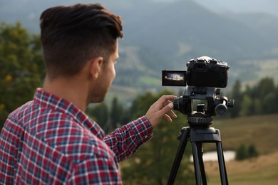 Photo of Man filming video with modern camera on tripod outdoors