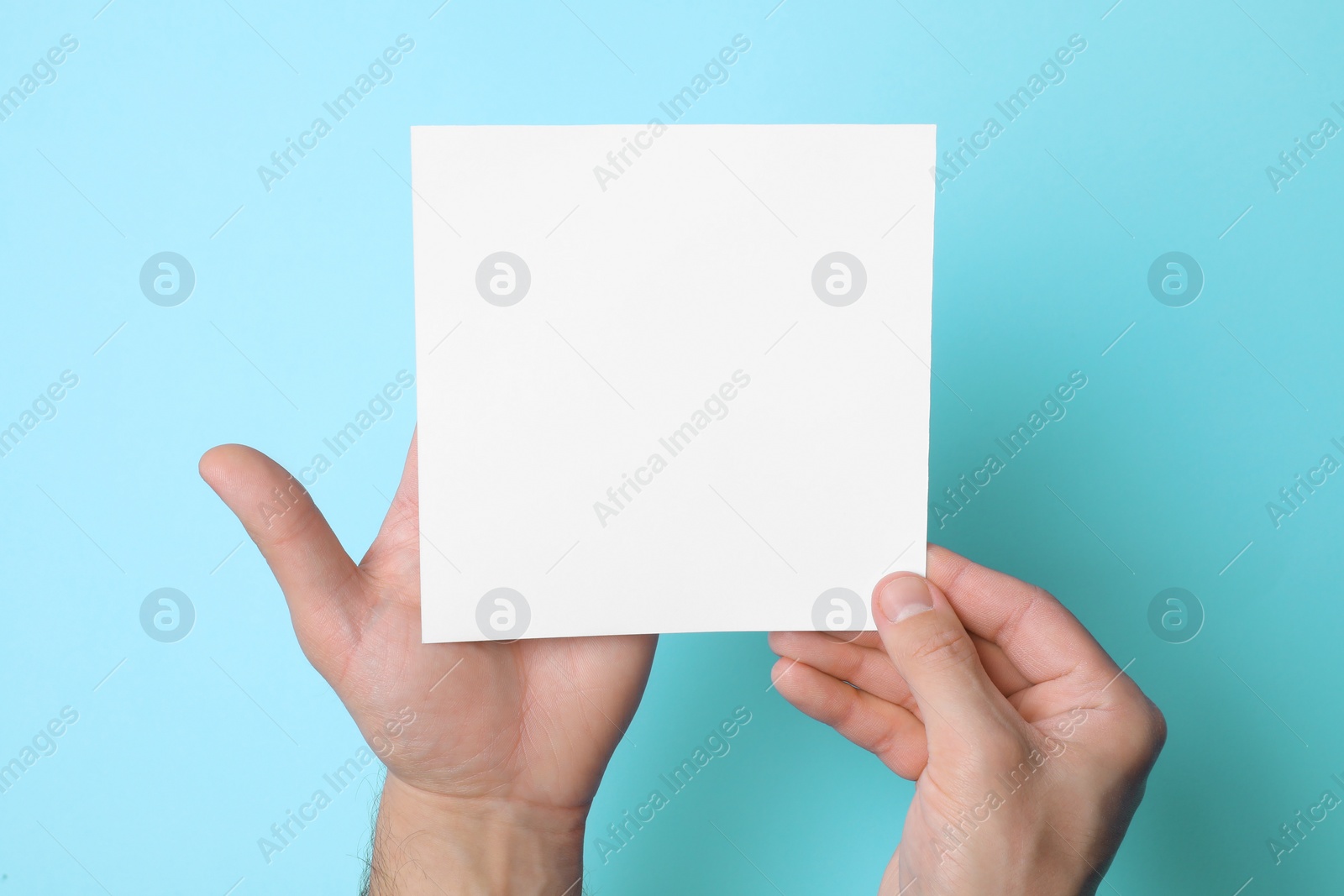 Photo of Man holding sheet of paper on light blue background, top view. Mockup for design