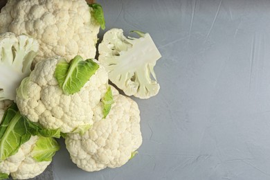 Fresh whole and cut cauliflowers on light grey table, top view. Space for text