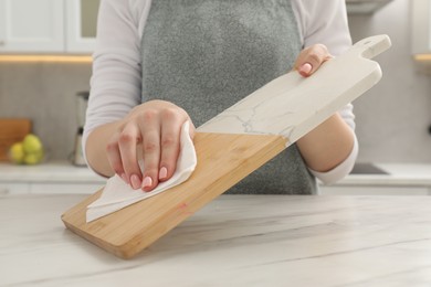 Photo of Woman wiping cutting board with paper napkin at white table, closeup