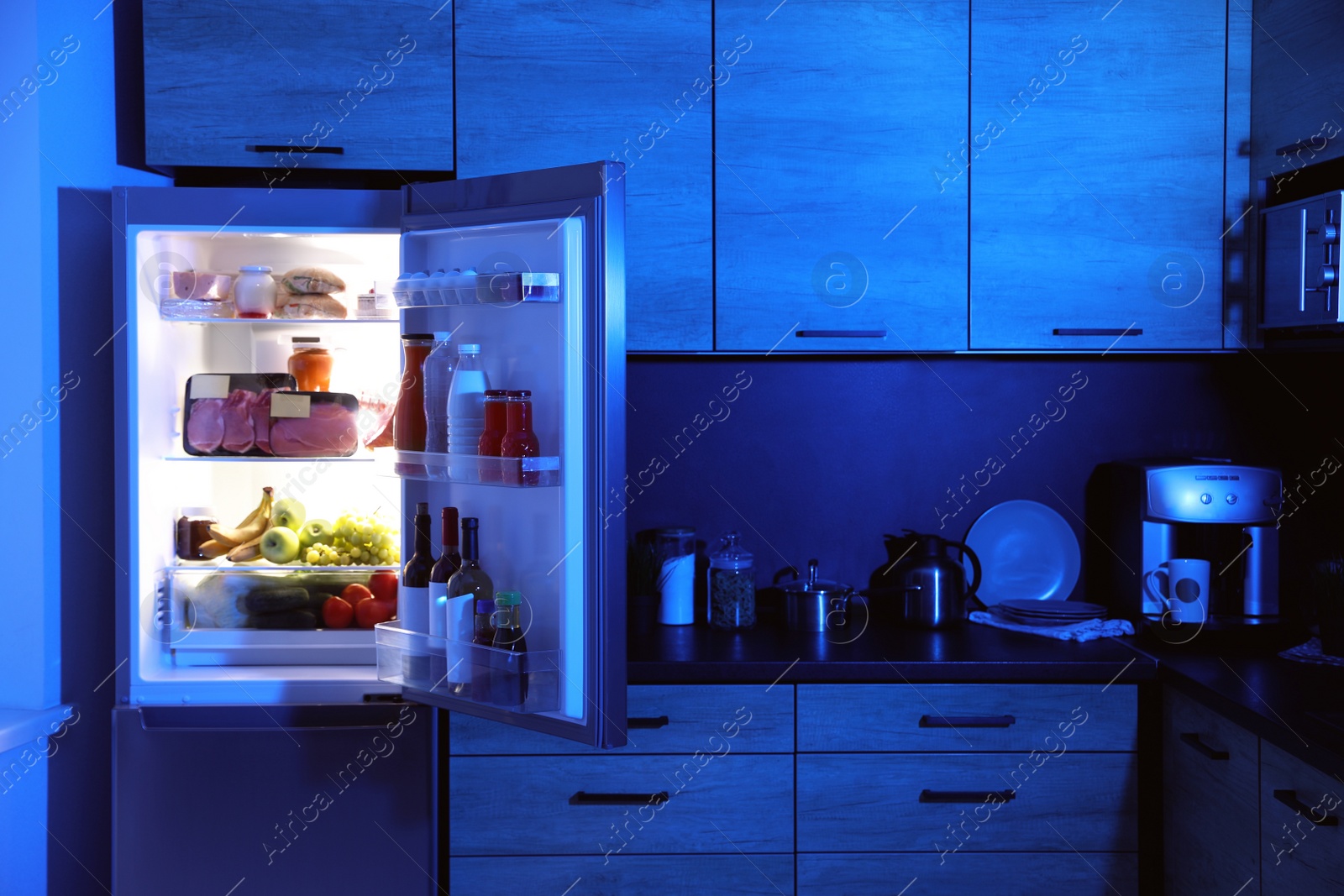 Photo of Open refrigerator full of products in kitchen at night