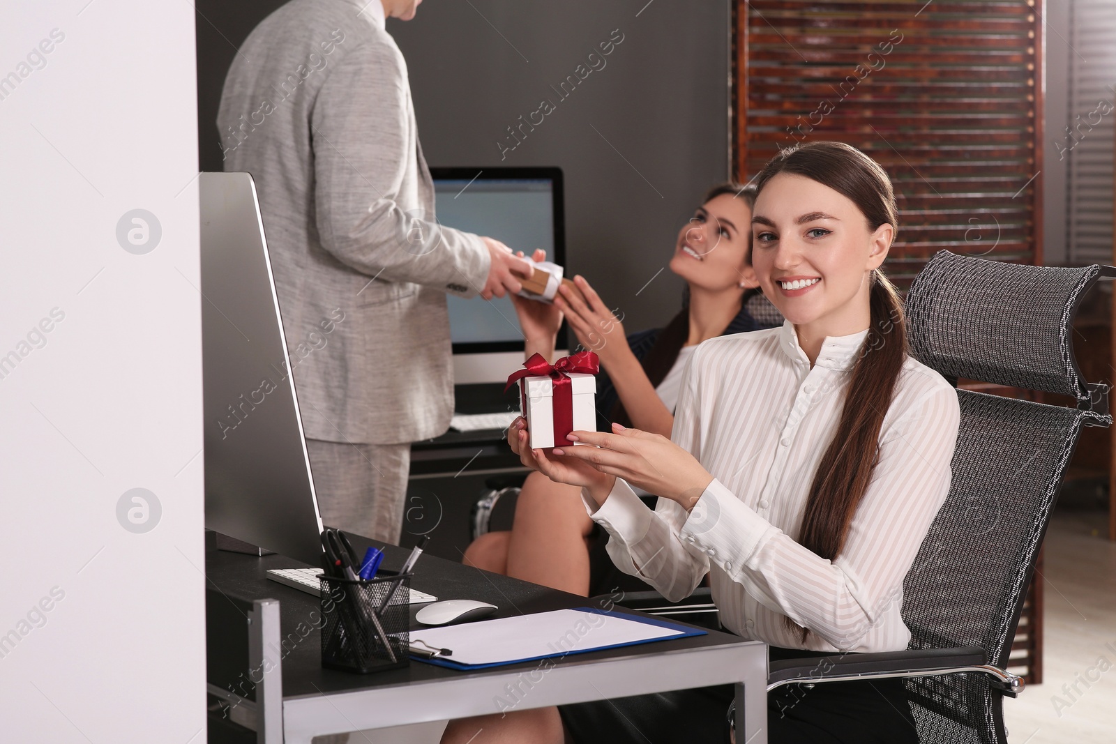 Photo of Happy woman holding festive box and man presenting gift to his colleague in office