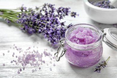 Photo of Natural sugar scrub and lavender flowers on white wooden table, space for text. Cosmetic product
