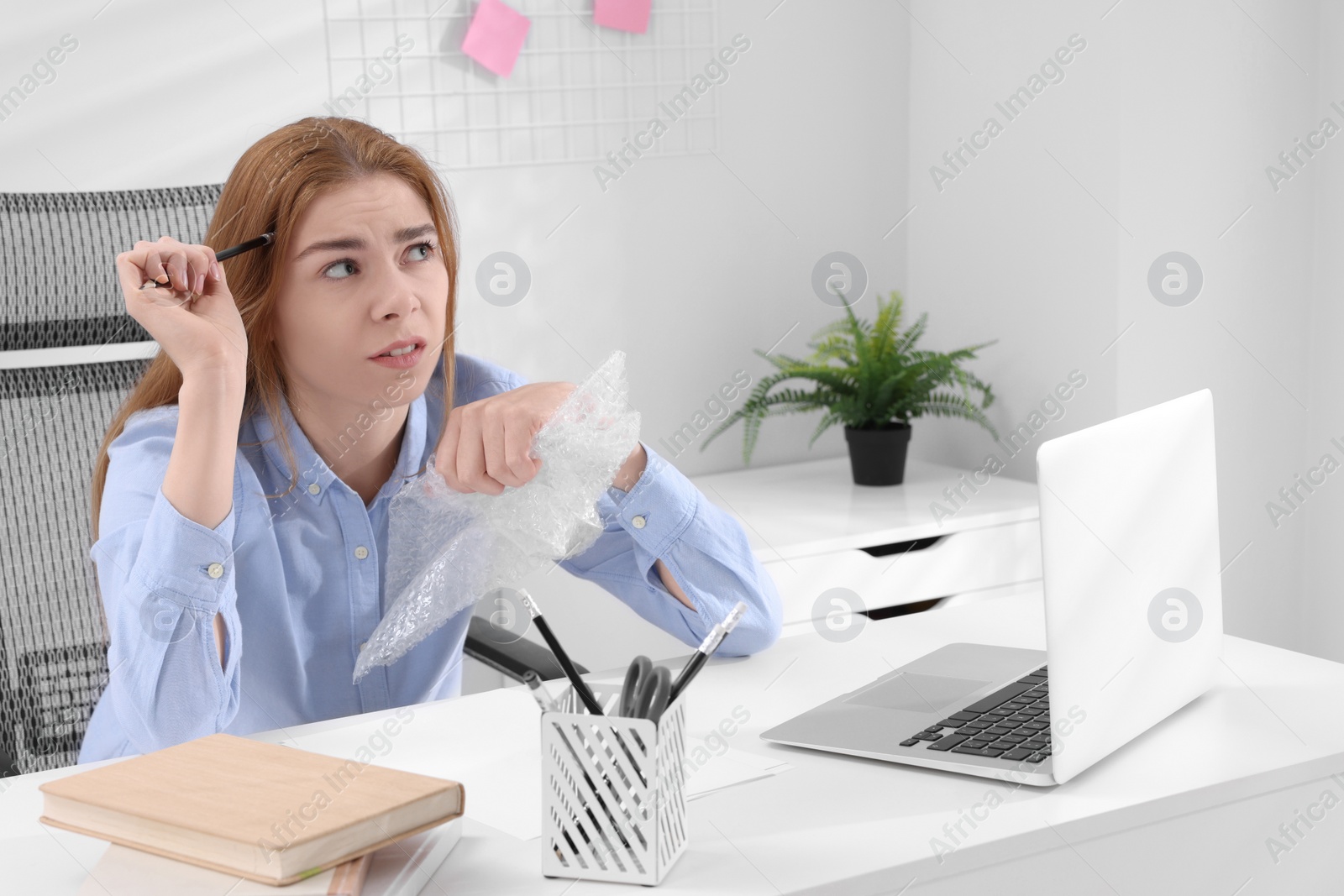 Photo of Woman popping bubble wrap at desk in office, space for text. Stress relief