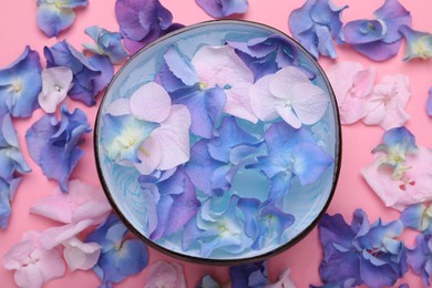 Spa composition. Aromatic water in bowl and flowers on pink background, flat lay