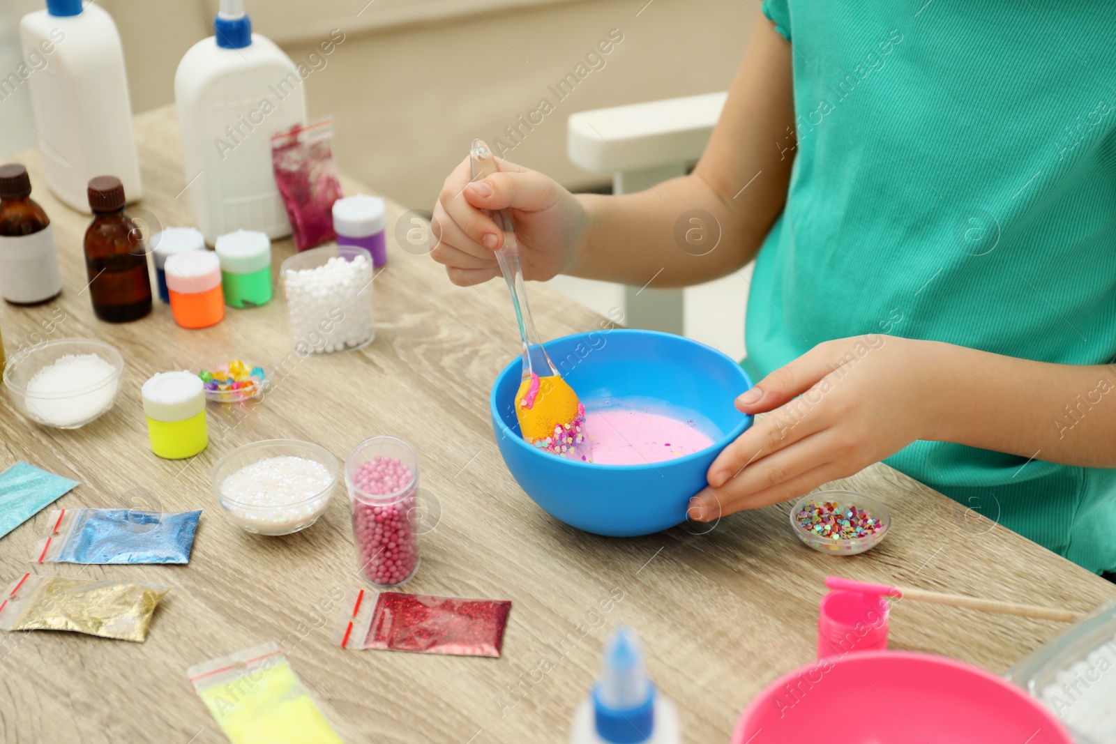 Photo of Little girl mixing ingredients with silicone spatula at table, closeup. DIY slime toy