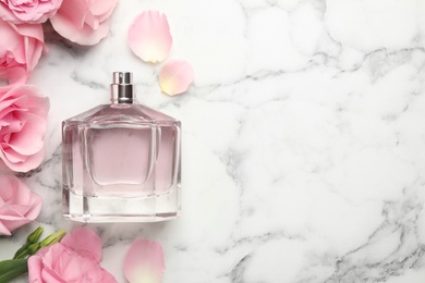 Photo of Bottle of perfume, beautiful flowers and petals on white marble table, flat lay. Space for text