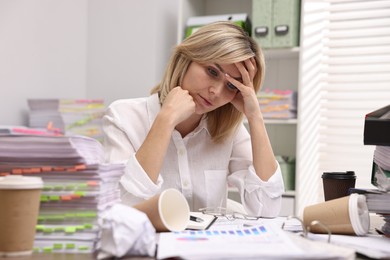 Photo of Overwhelmed woman surrounded by documents and paper coffee cups at workplace in office