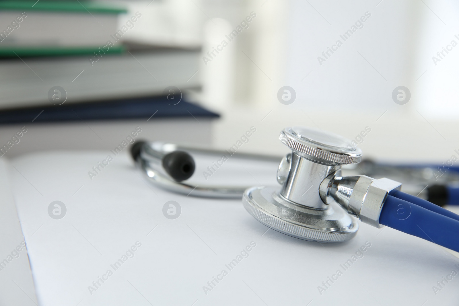 Photo of One new medical stethoscope and books on white table, closeup