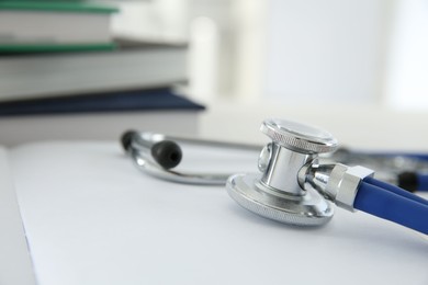 One new medical stethoscope and books on white table, closeup