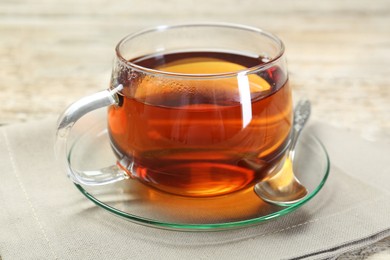 Photo of Aromatic tea in glass cup, spoon and napkin on wooden table