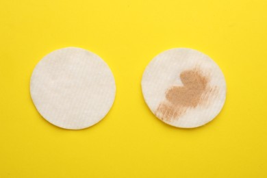 Photo of Clean and dirty cotton pads after removing makeup on yellow background, flat lay