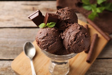 Tasty chocolate ice cream with mint in glass dessert bowl served on wooden table, closeup