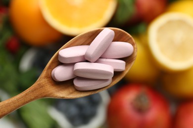 Photo of Vitamin pills in spoon over fresh fruits, top view