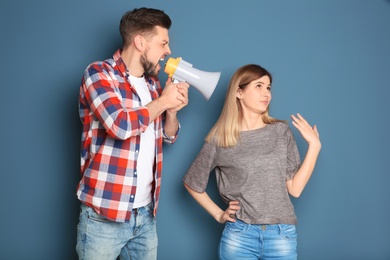 Photo of Young man with megaphone shouting at woman on color background