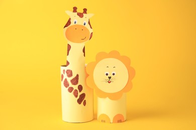 Photo of Toy giraffe and lion made from toilet paper hubs on yellow background. Children's handmade ideas