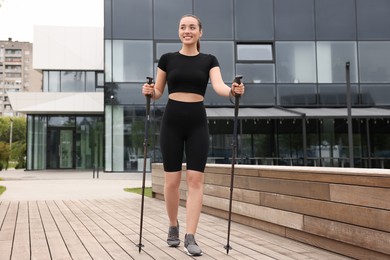 Photo of Young woman practicing Nordic walking with poles outdoors