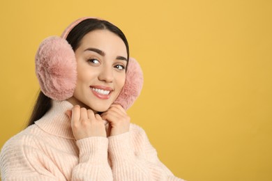 Photo of Beautiful young woman wearing earmuffs on yellow background. Space for text