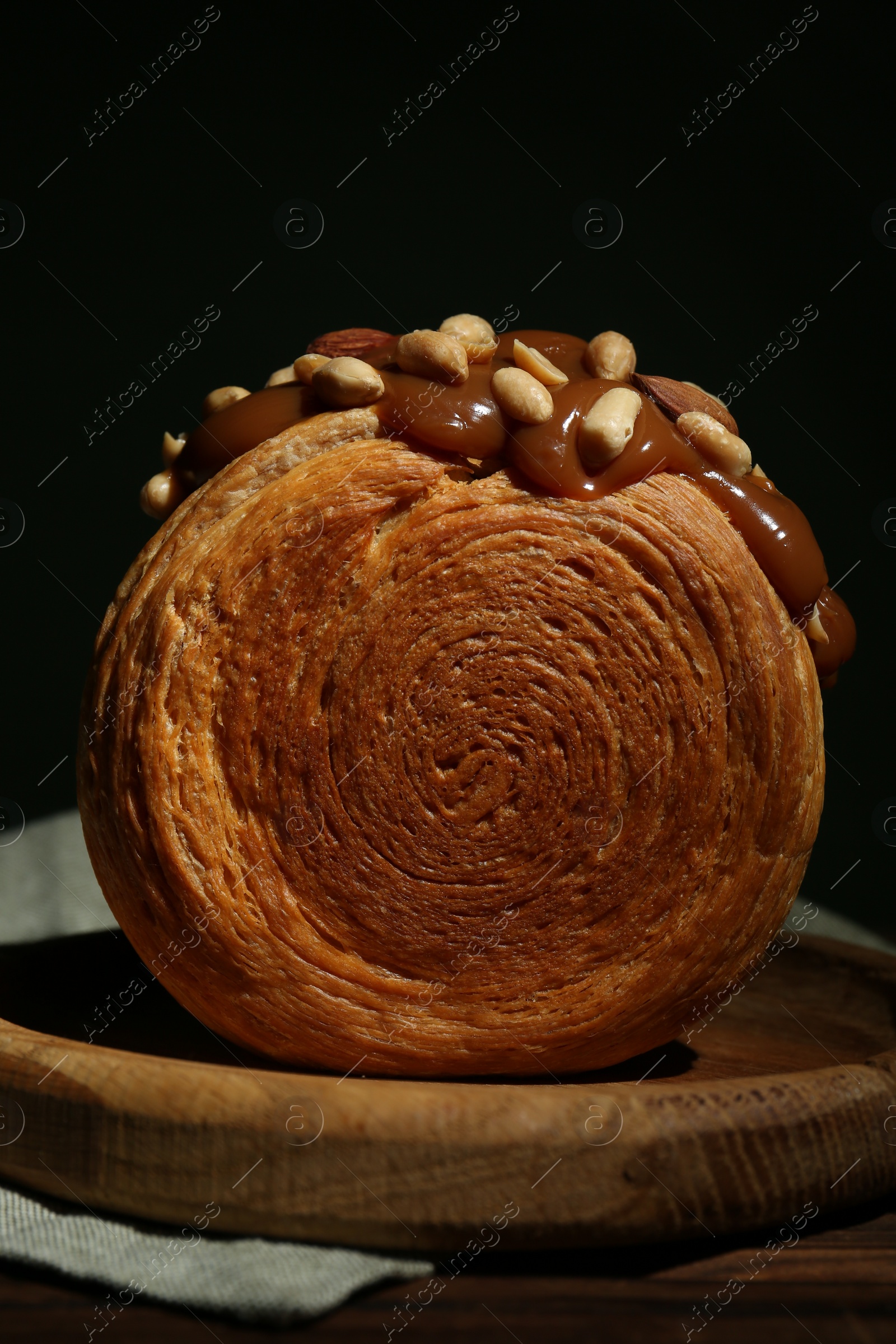 Photo of Round croissant with chocolate paste and nuts on wooden table, closeup. Tasty puff pastry