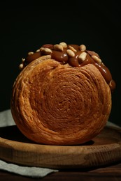 Round croissant with chocolate paste and nuts on wooden table, closeup. Tasty puff pastry