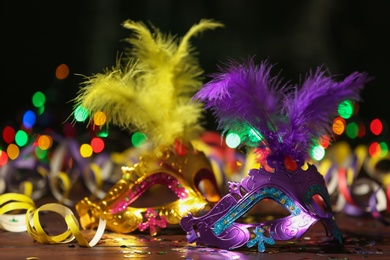 Photo of Beautiful carnival masks and party decor on table against blurred lights