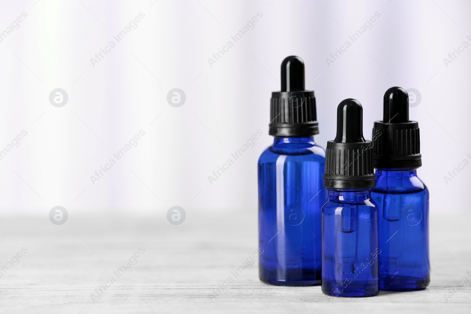 Photo of Bottles of essential oils on table against light background, space for text. Cosmetic products