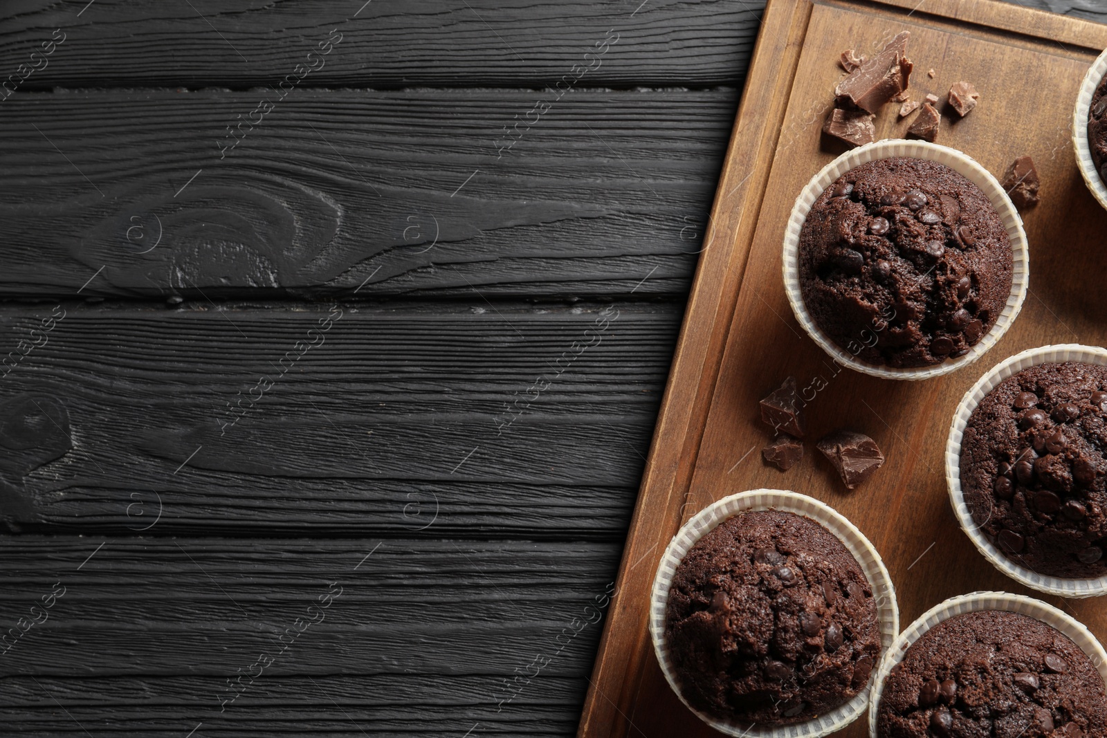 Photo of Delicious chocolate muffins on black wooden table, top view. Space for text