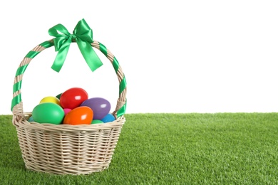 Photo of Wicker basket with Easter eggs on green grass against white background. Space for text