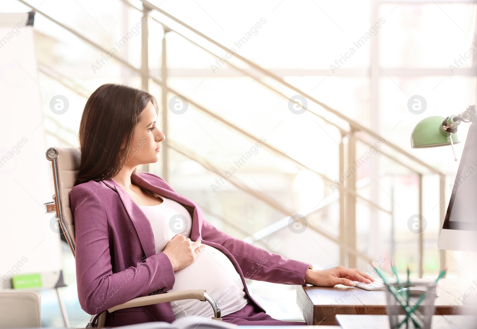 Photo of Young pregnant woman working with computer at table in office