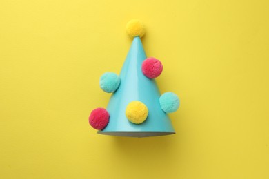 Photo of One light blue party hat with pompoms on yellow background, top view