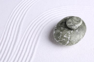 Photo of Zen garden stones on white sand with pattern. Space for text