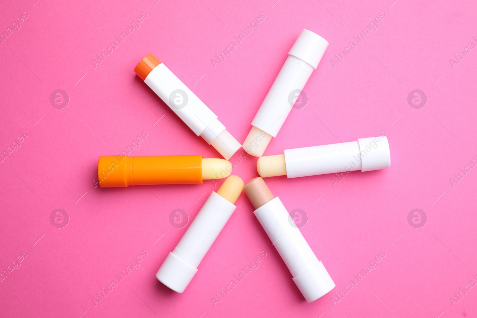 Photo of Hygienic lipsticks on pink background, flat lay