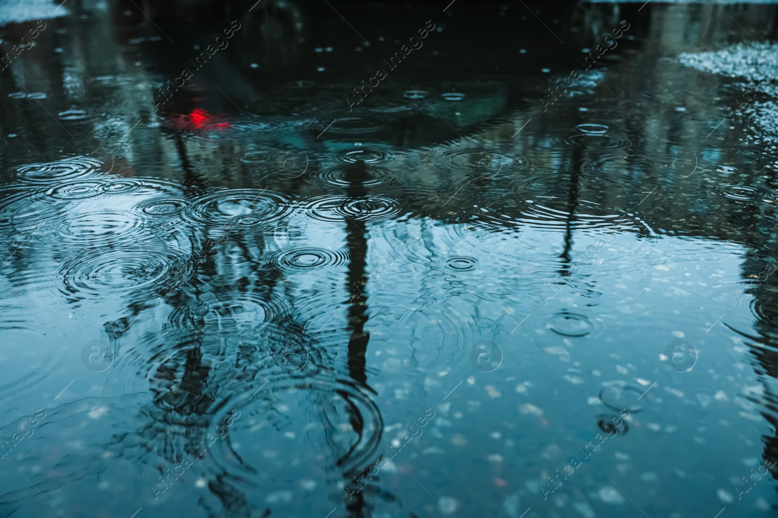 Photo of Rain drops falling down onto puddle outdoors