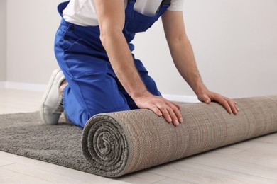 Photo of Worker unrolling new carpet on floor in room, closeup
