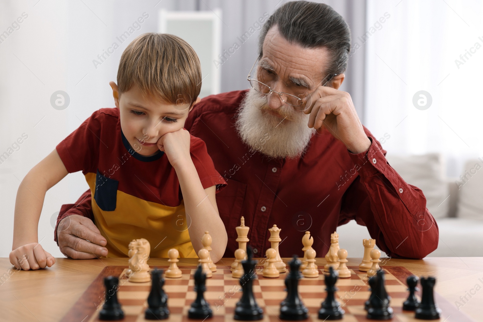 Photo of Senior man teaching his grandson to play chess at home