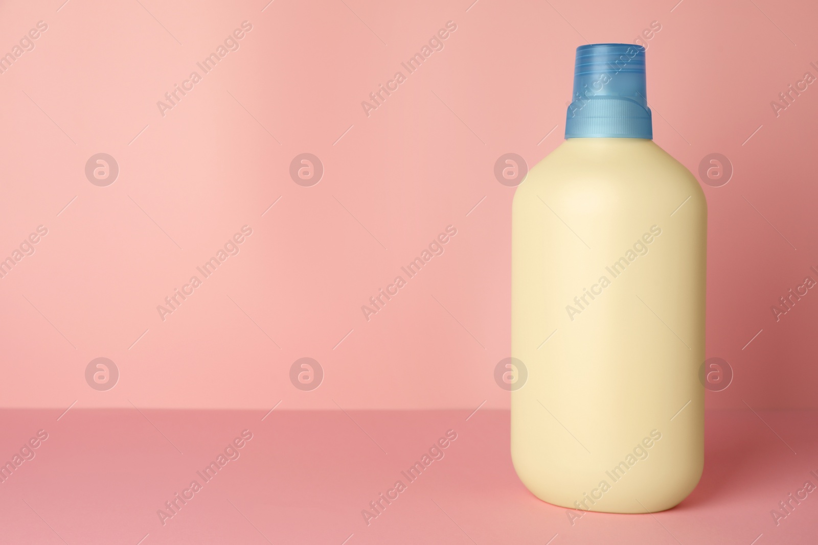 Photo of Bottle of fabric softener on pink background, space for text