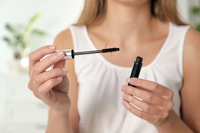 Woman holding mascara and brush with fallen eyelashes indoors, closeup