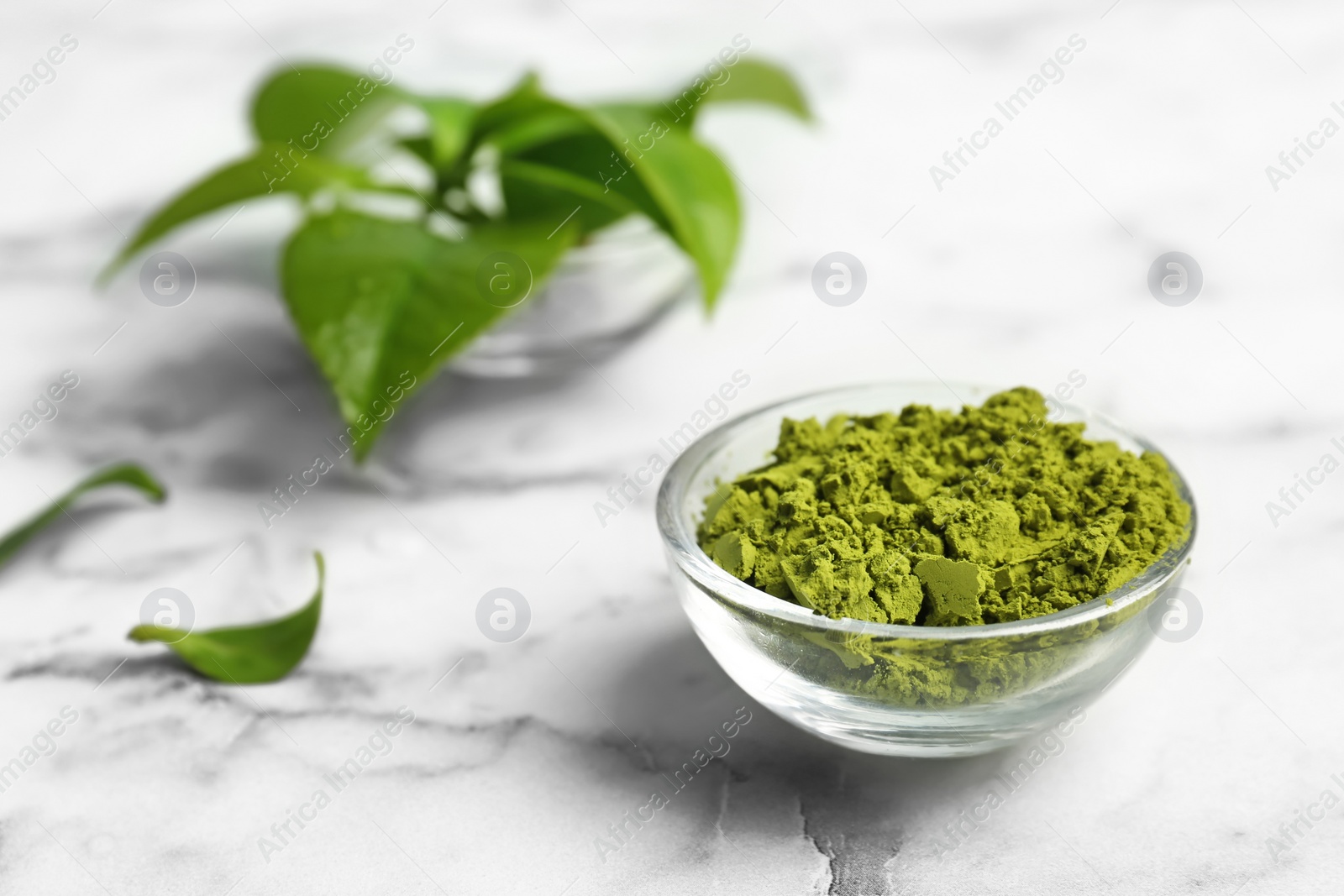 Photo of Bowl with matcha tea and green leaves on marble table