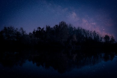 Image of Amazing starry sky and trees reflecting in lake at night